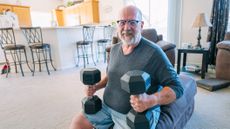 Man sitting in living room with heavy dumbbells on his knees