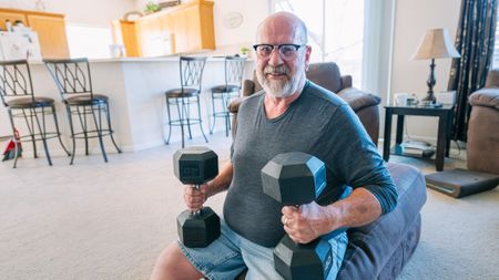 Man sitting in living room with heavy dumbbells on his knees