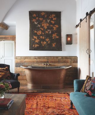 Rustic bathroom within a bedroom with copper bath and wood floor