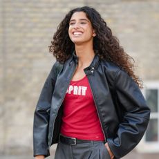 woman with long curly brown hair wearing black leather jacket and red tank top