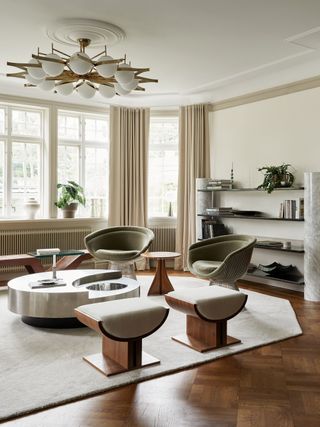 living room with armchairs, ottomans, a daybed, round coffee table, wall shelves, modern pendant light, and angled rug on floor