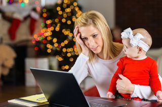 busy mum at computer holding daughter at Christmas