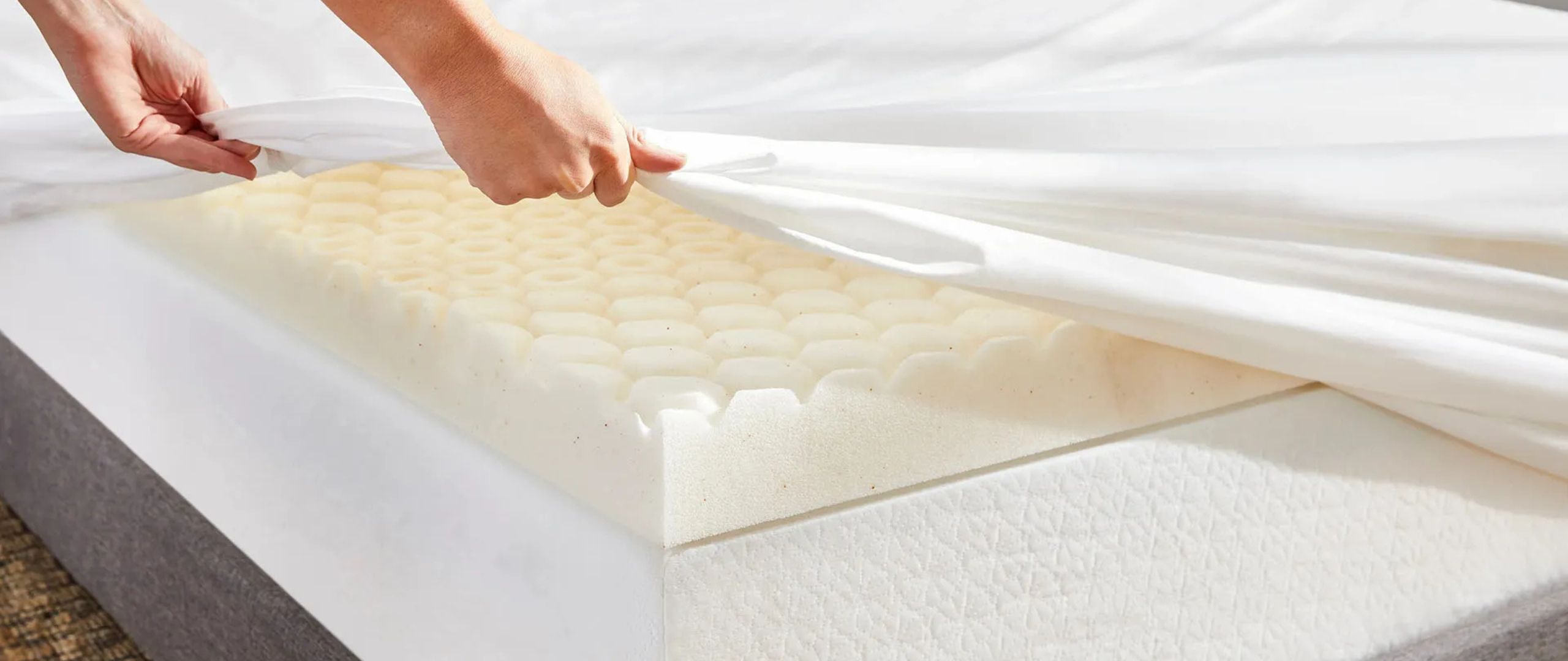 A woman&#039;s hands covers the Molecule CopperWELL Mattress Topper with a white sheet.