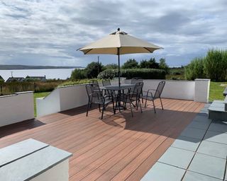 Teak and light brown composite decking outside with patio dining set and beige garden parasol decor