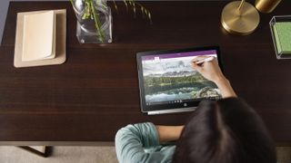 En kvinna sitter vid ett skrivbord och skriver på en HP Chromebook X2-skärm med hjälp av en stylus.