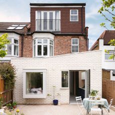 broken plan kitchen design rear exterior of an extended semi-detached house with pale white brick facade and a bistro set on the patio