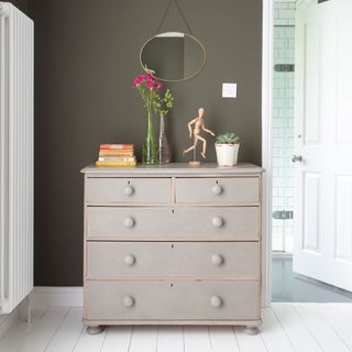 Grey painted drawers in bedroom with grey walls next to open bathroom door