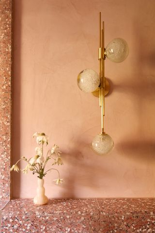 A space with salmon pink walls and a gold lighting fixture