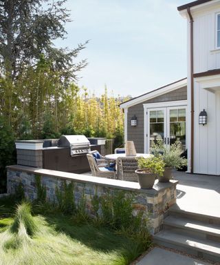 Coastal-inspired small back yard landscaping ideas with long grasses and a seating area with barbecue up a few steps behind a stone wall.