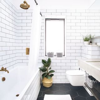 bathroom with white metro tiles on wall, brass shower head over bath and potted plant
