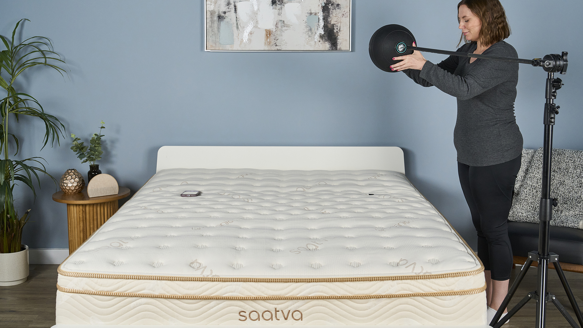 A Tom&#039;s Guide mattress tester stands at the edge of a hybrid mattress, on the right hand side, holding a 5kg slam ball ready to let it fall (without exerting any of her own force onto it). This is the first step in our motion isolation slam ball and accelerometer test, devised to measure how much of the initial impact of movement the mattress absorbs and how quickly it stops it