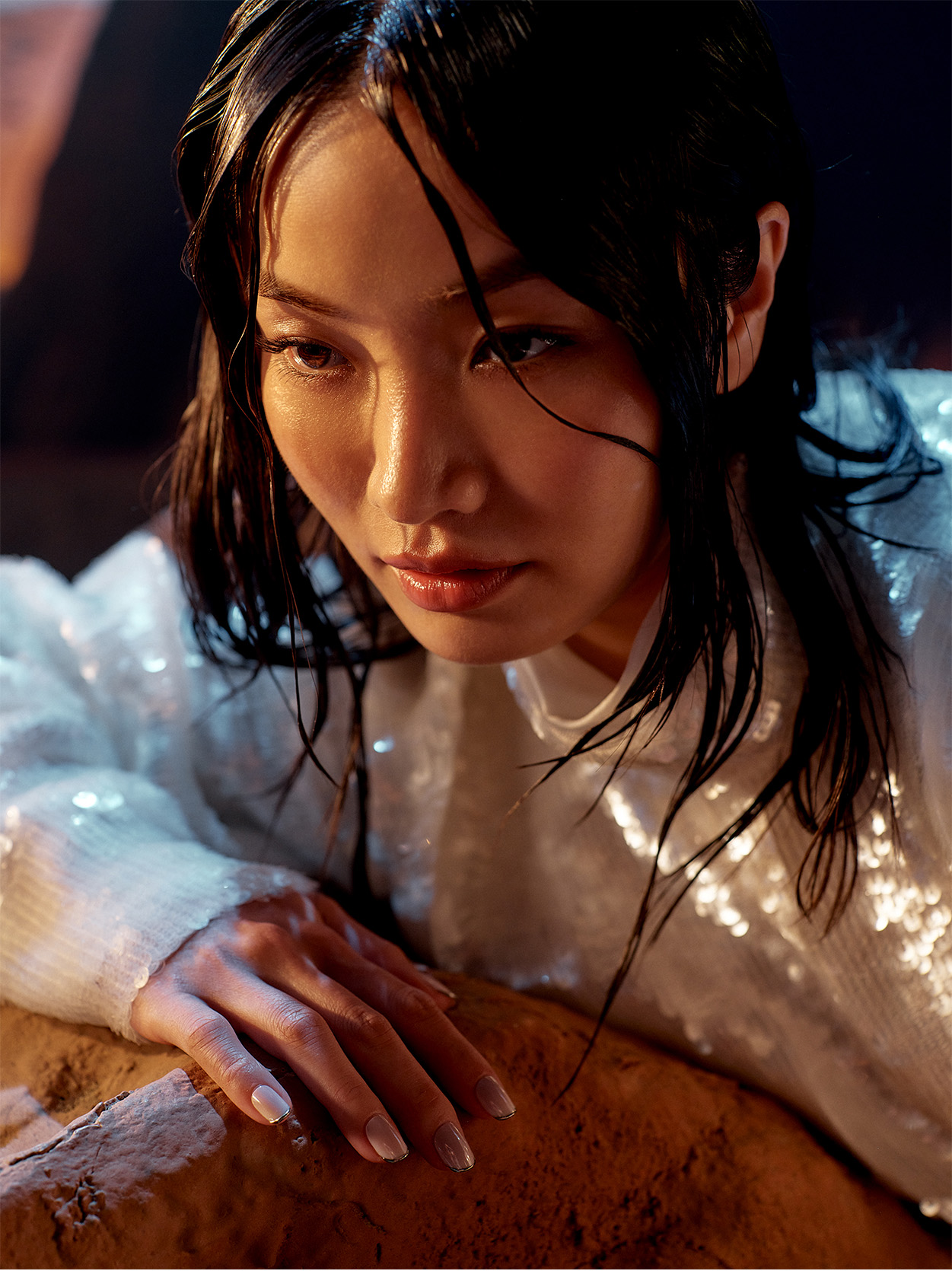 Close-up of Anna Sawai leaning on a rock in a shimmering white outfit.