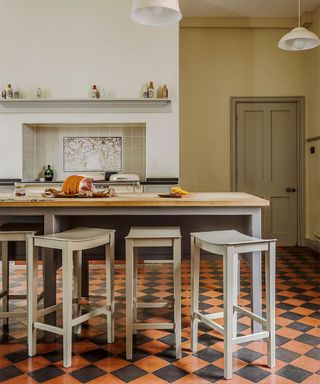 A kitchen with greige and wood island and red and black checkered tile flooring