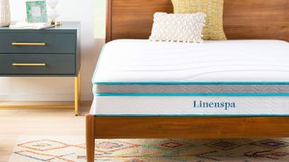The Linenspa mattress on a wooden frame placed next to a black and gold bedside table