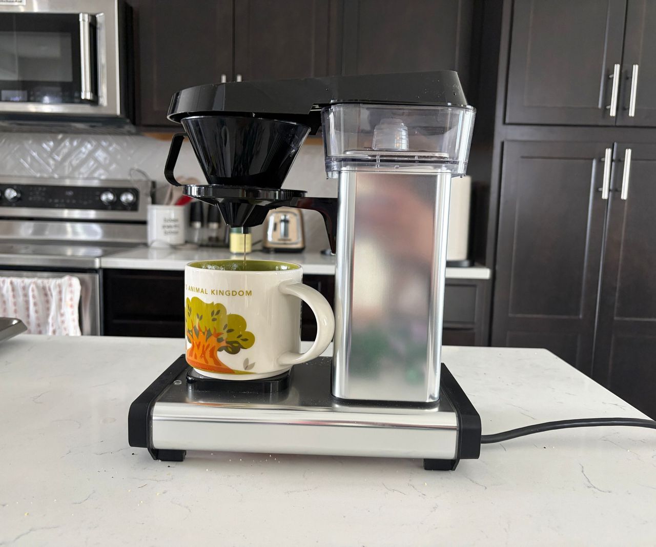 A silver moccamaster cup one coffee maker, with a large mug underneath the drip spout.