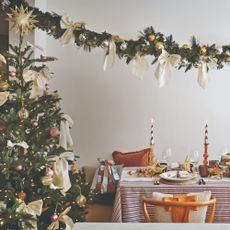 A Christmas-decorated dining room with a garland above the table and a Christmas tree to the side of it