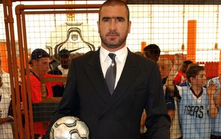 Eric Cantona wearing a suit and holding a football.