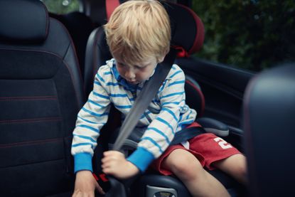 young boy in car seat fastening seatbelt