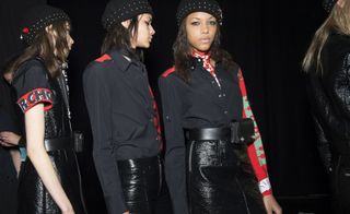 Models backstage wearing black skirts with black and red buttoned shirts