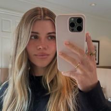 Sofia Richie Grainge wearing a black crewneck sweatshirt in a mirror selfie with her pink phone case.