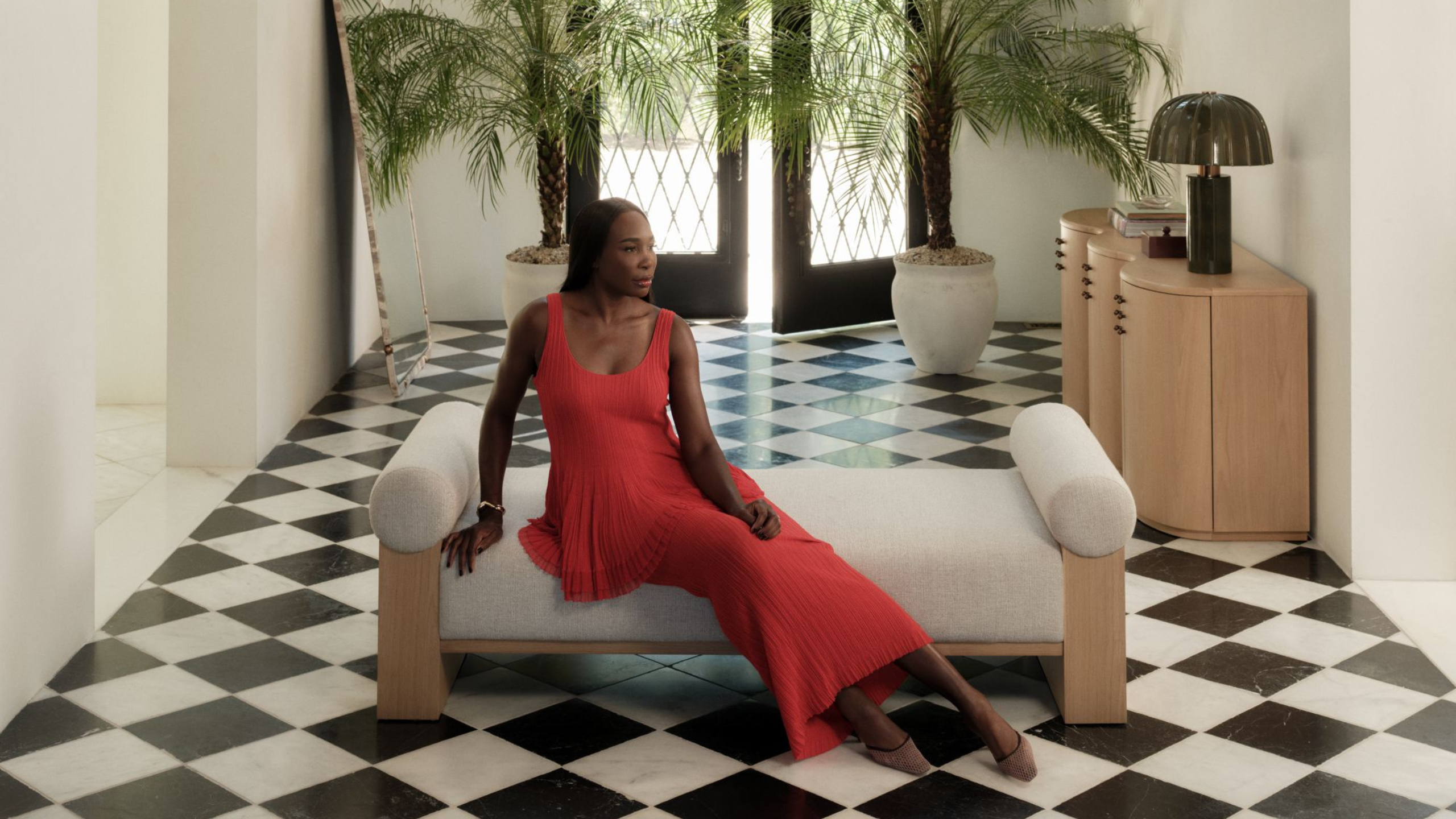 a woman in a red dress sitting on a chaise lounge in a foyer with checkered floors