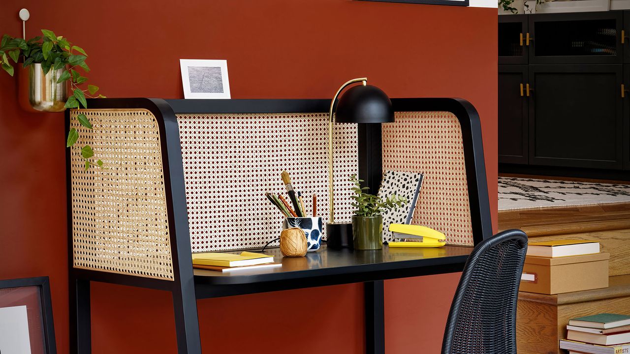 Rattan black and beige desk in home office next to rust wall.