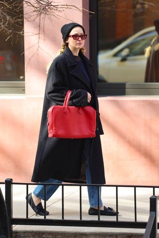 Jennifer Lawrence walks in new york city wearing the boat shoe trend with a black coat and red bag