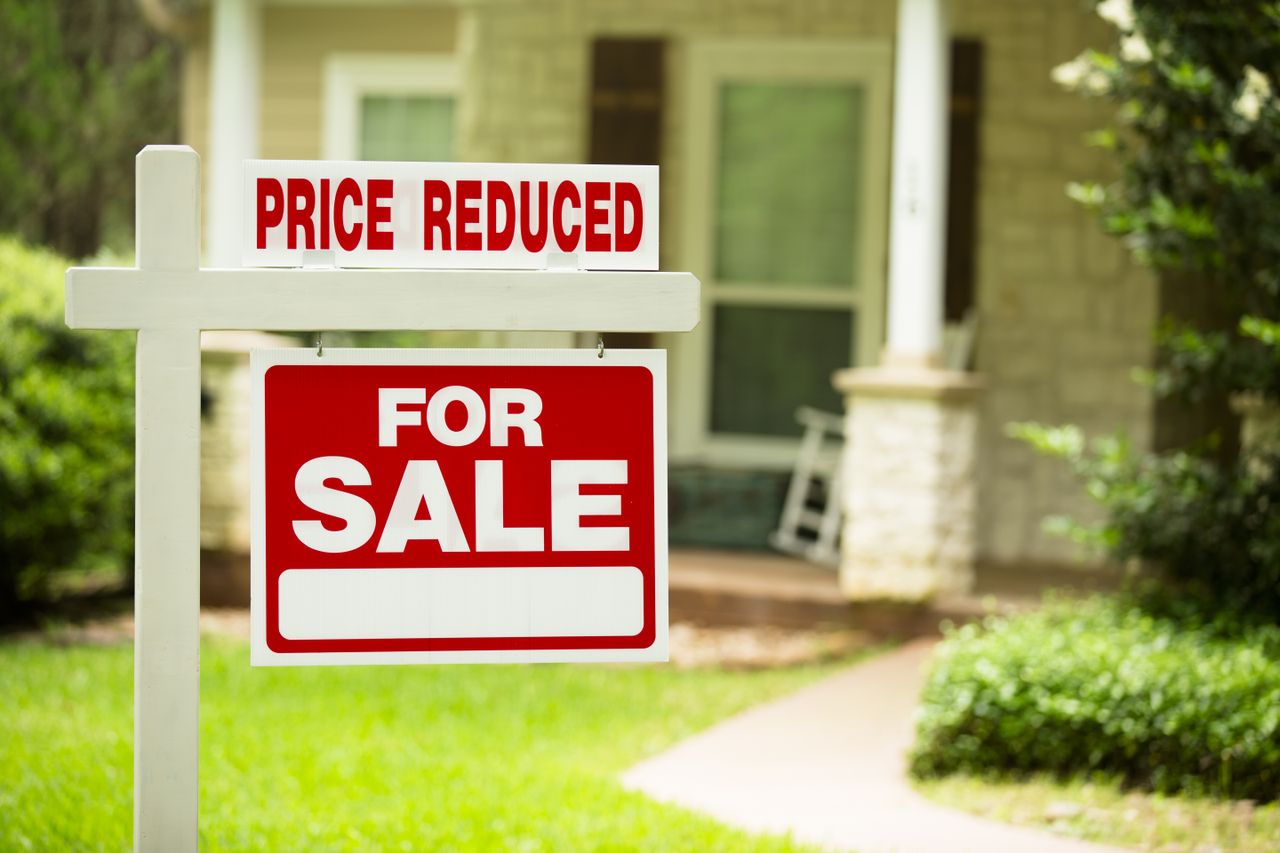 Image of a sign reading &quot;price reduced/for sale&quot; in front of a home. 