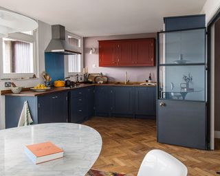 A contemporary U-shaped kitchen with blue and red cabinetry and pale plaster pink statement wall.