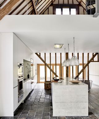Roundhouse sleek white kitchen in a historic barn with beams and cobbles stone floor
