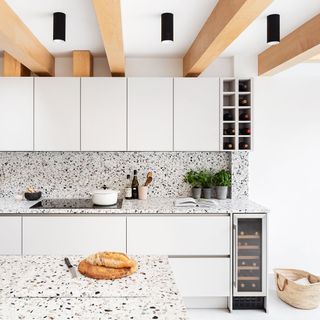 White kitchen with terrazzo splashback and worktops and an oak beamed ceiling