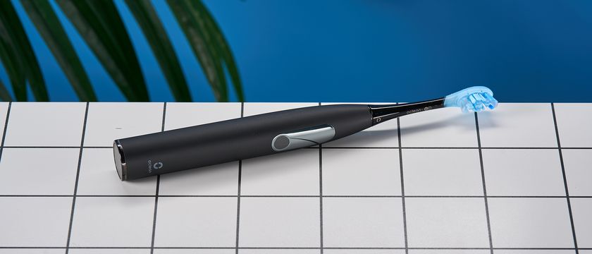 a black electric toothbrush Oclean X Ultra S with a small touchscreen and a blue toothbrush head and a square charging stand