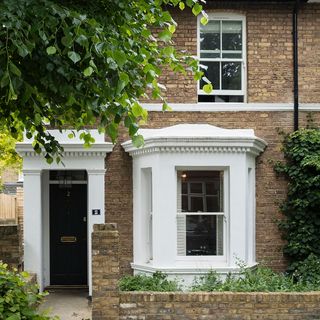 house with brick wall and white windows and black door with plants