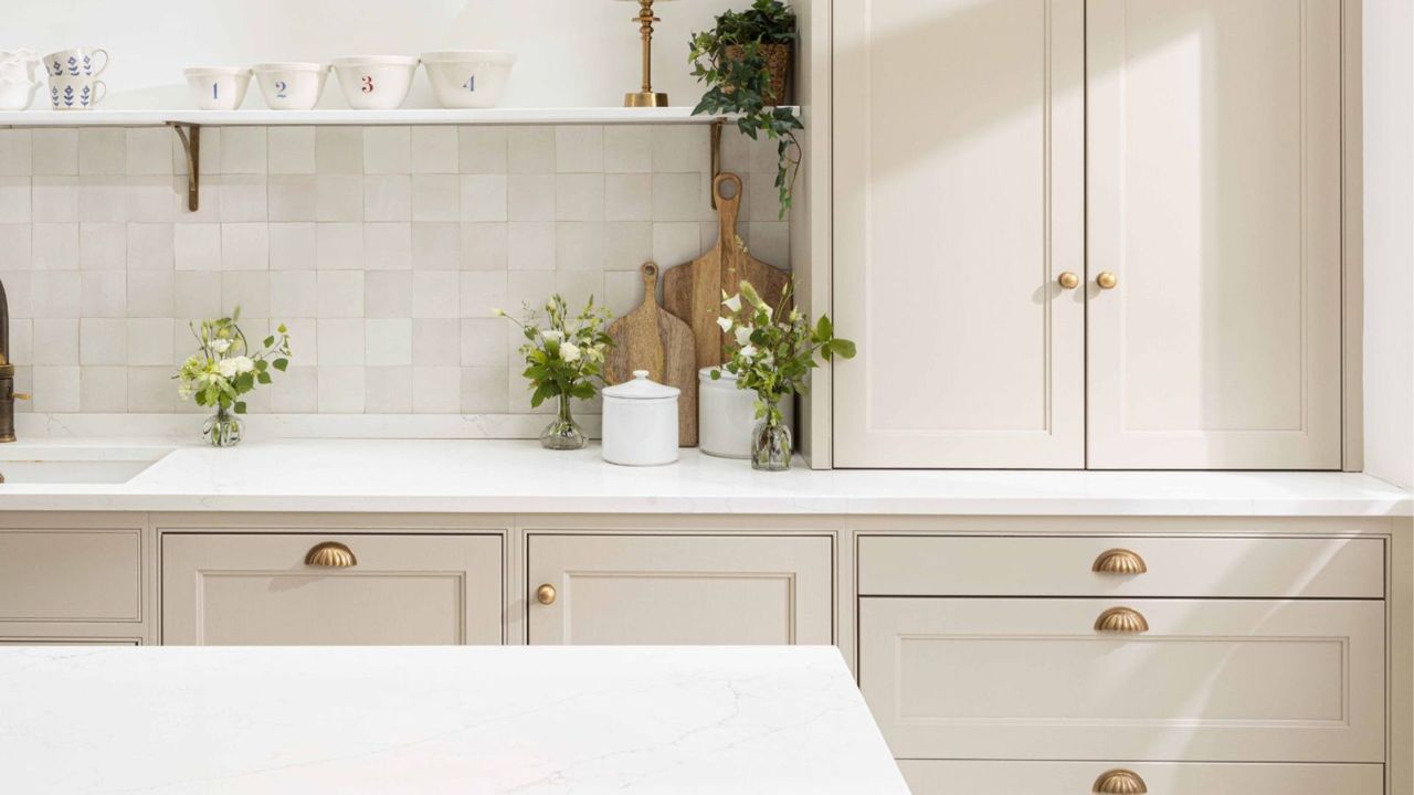 A neutral kitchen with brass cabinet and drawer handles, a marble splashback