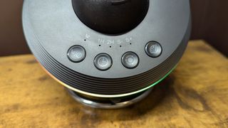 The Ainael Meteor and Galaxy Projector's four control buttons on a wooden table against a brown wall