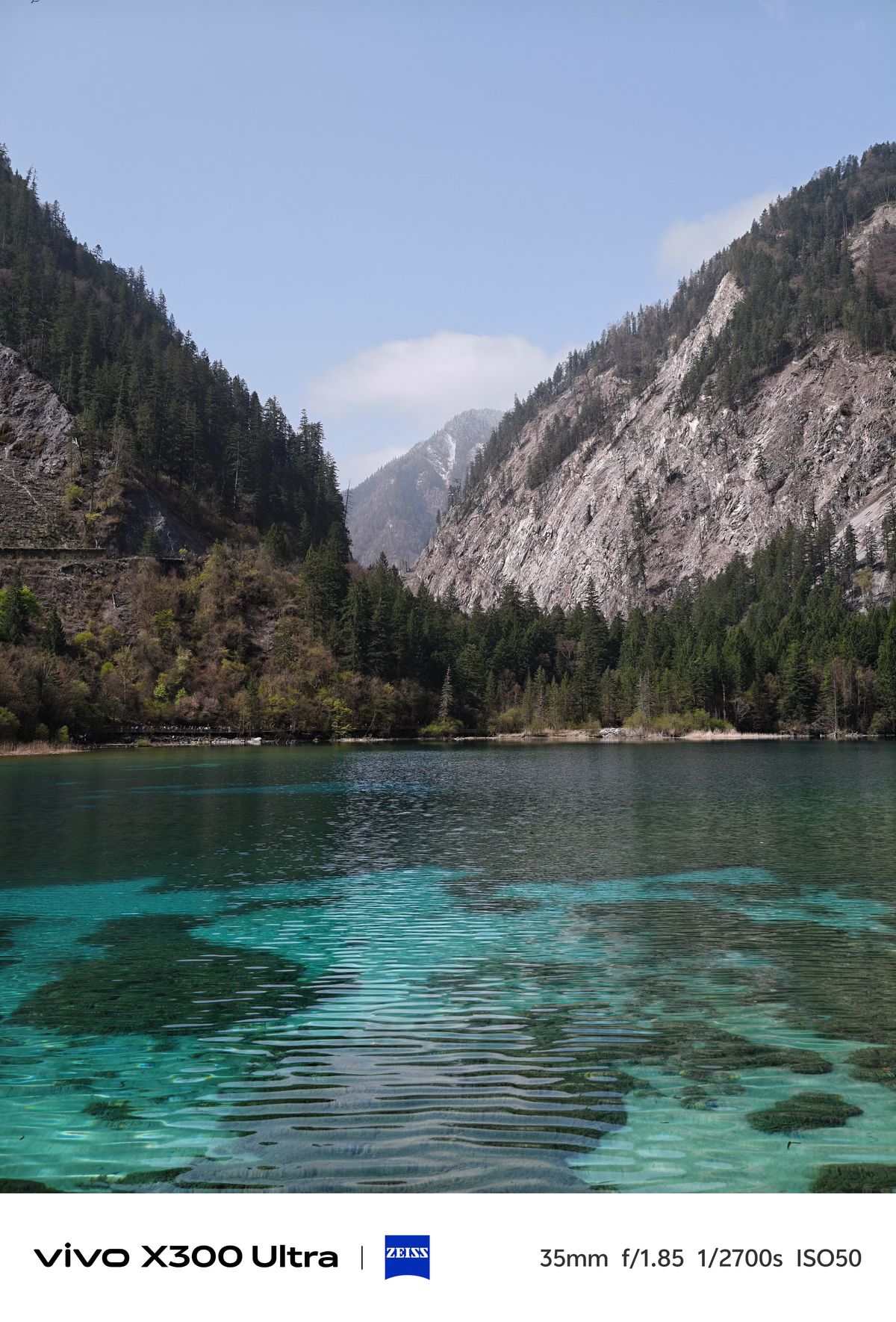 Rippling turquoise and blue water in an alpine lake bordered by steep rocky cliffs and pine trees.
