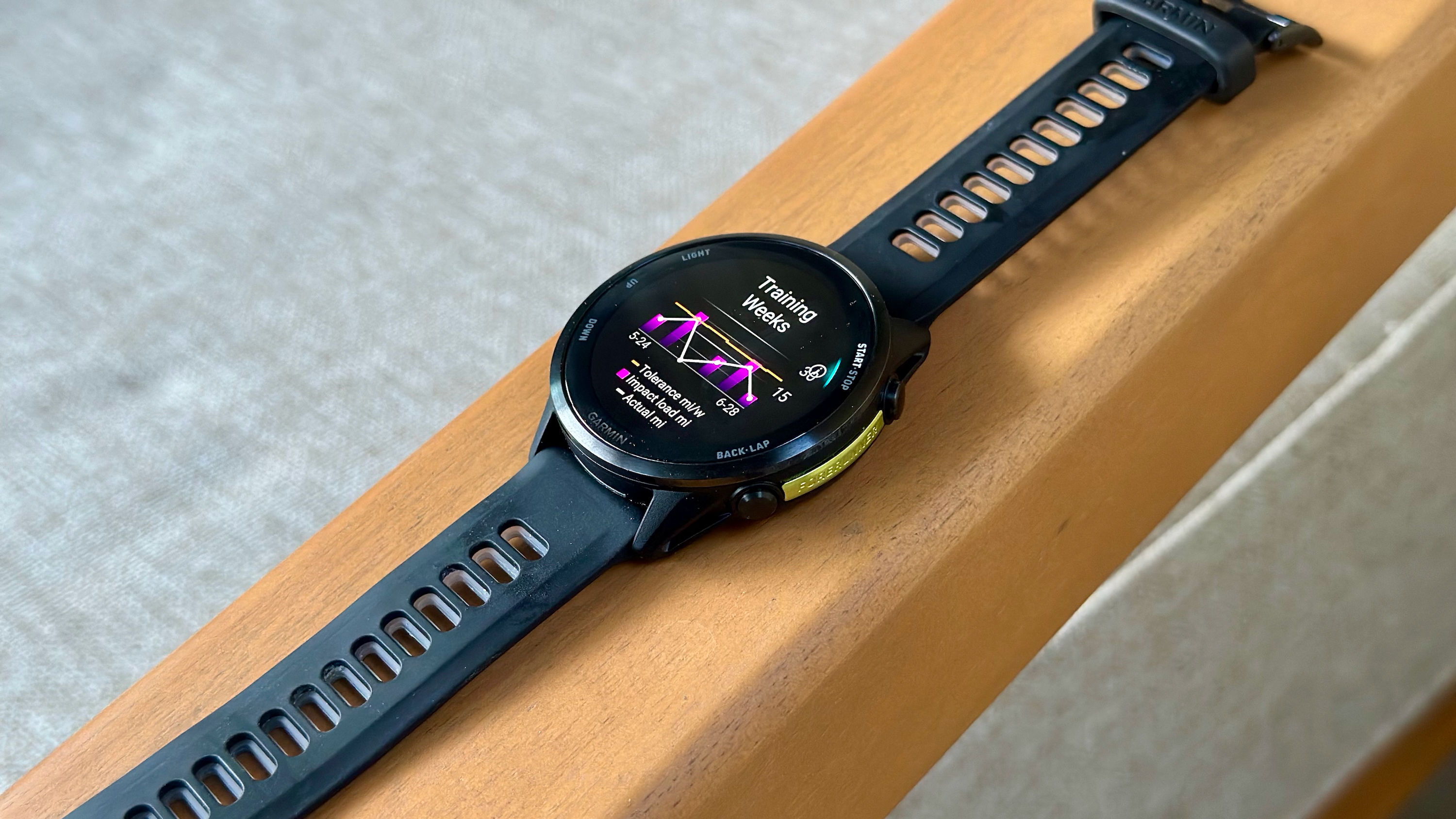 The Garmin Forerunner 970 sitting on an armrest showing the Training Weeks widget with running tolerance and impact load.