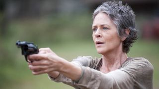Melissa McBride as Carol, holding a gun in front of her looking shocked in "The Walking Dead" season 4 episode 14, titled "The Grove"