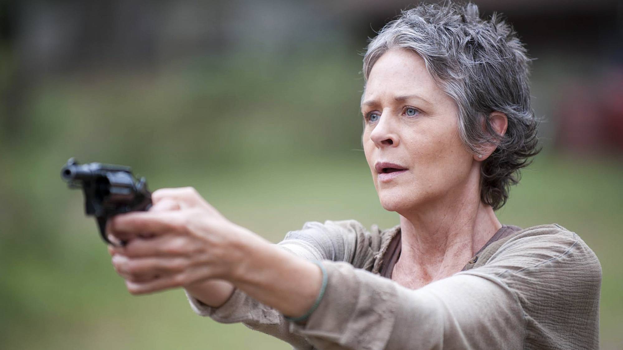 Melissa McBride as Carol, holding a gun in front of her looking shocked in "The Walking Dead" season 4 episode 14, titled "The Grove"