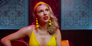 Taylor Swift wearing yellow earring and dress and playing the guitar in the Lover music video
