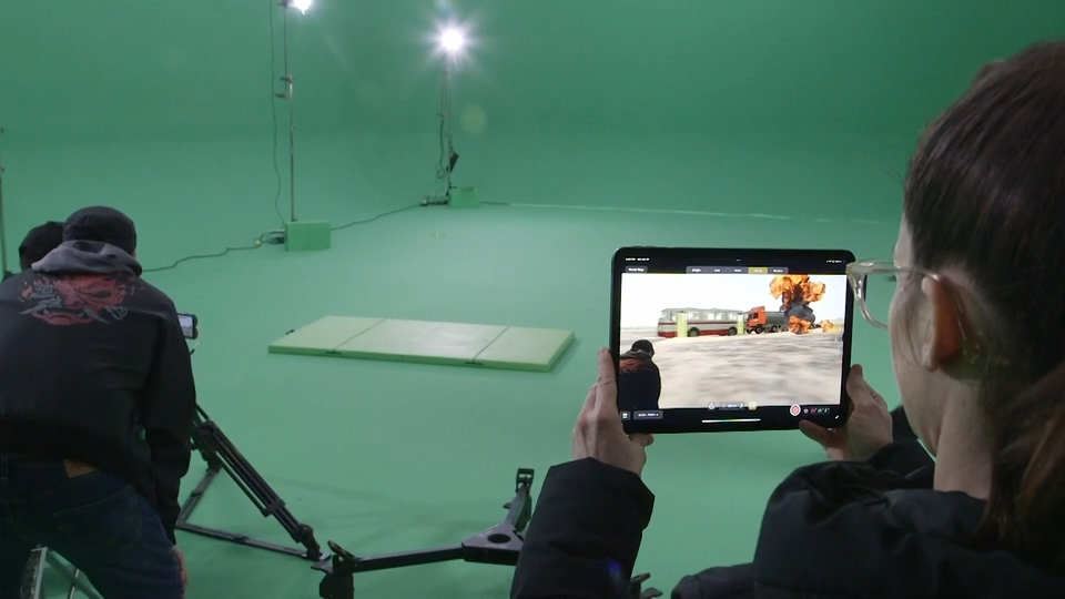 A person holds up an iPad on a green screen set