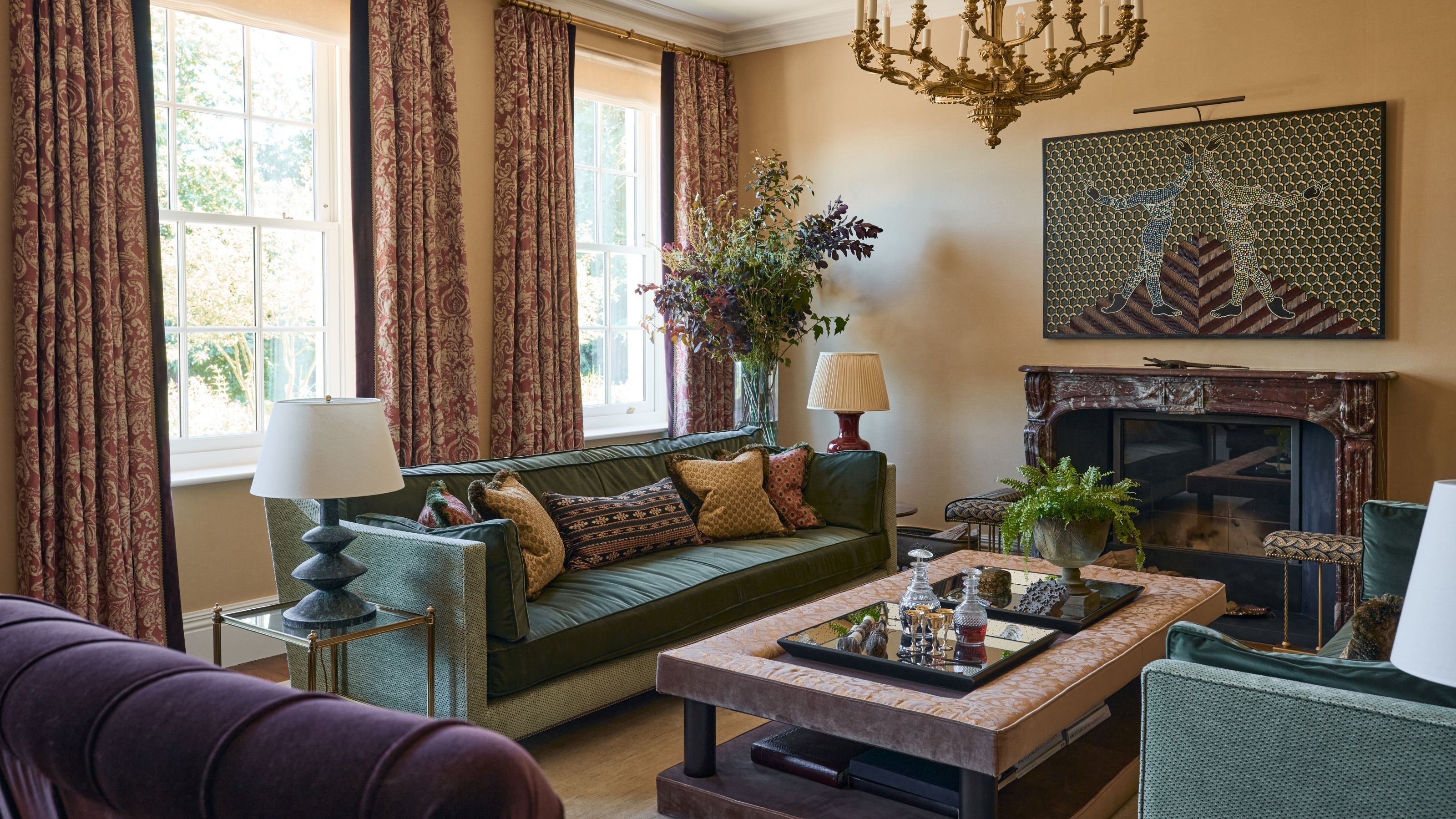 a warm living room with double windows and vintage style drapes, antique dark red marble fireplace, two green sofas and a concealed tv behind modern art