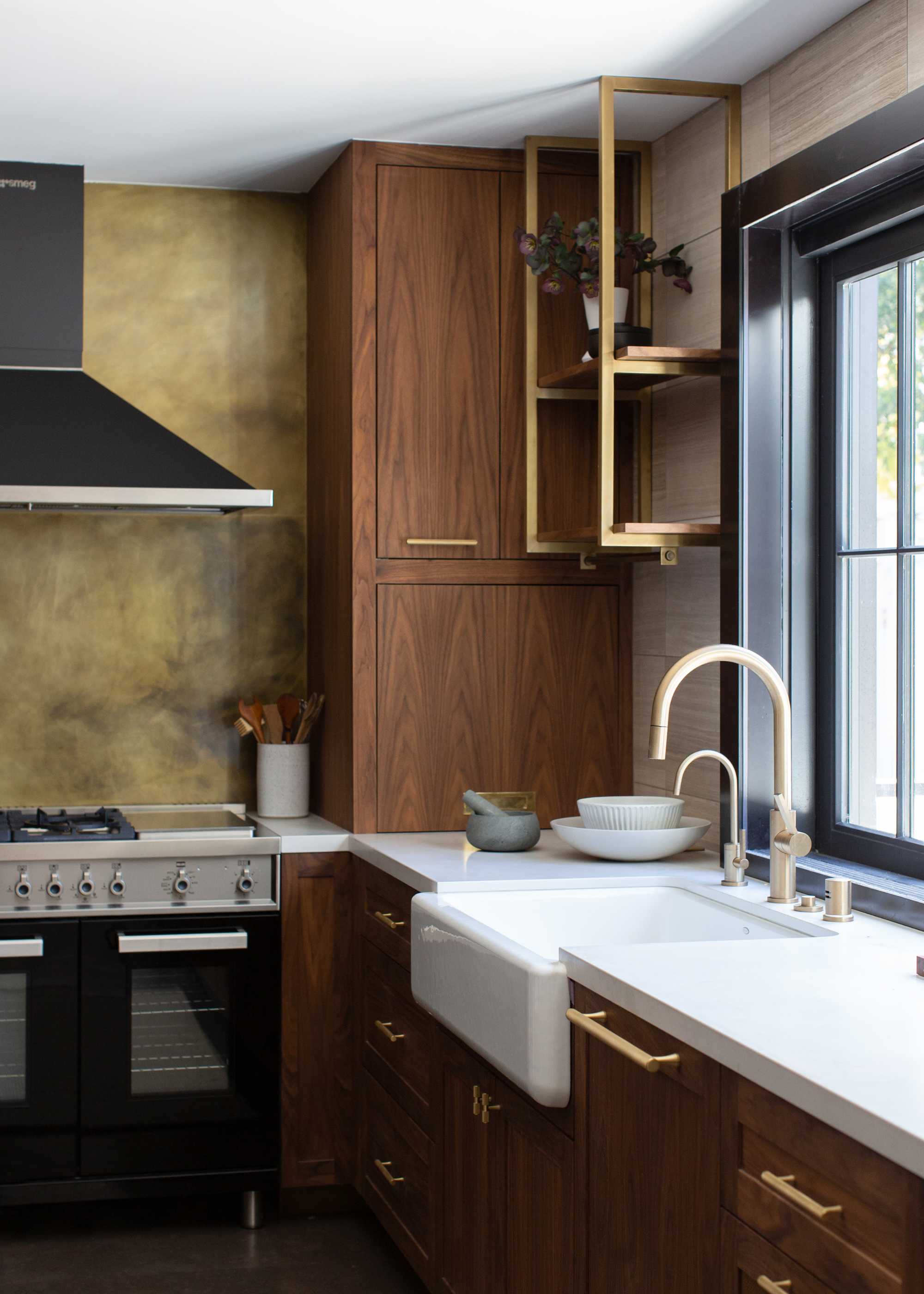 A kitchen with wood cabinets, a green limestone wall and gold hardware