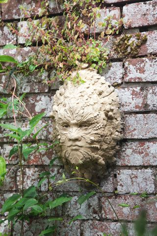 Green man sculpture on wall in small garden