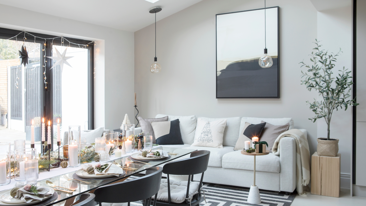 Black and white themed room with glass dining table decorated with white candles and greenery