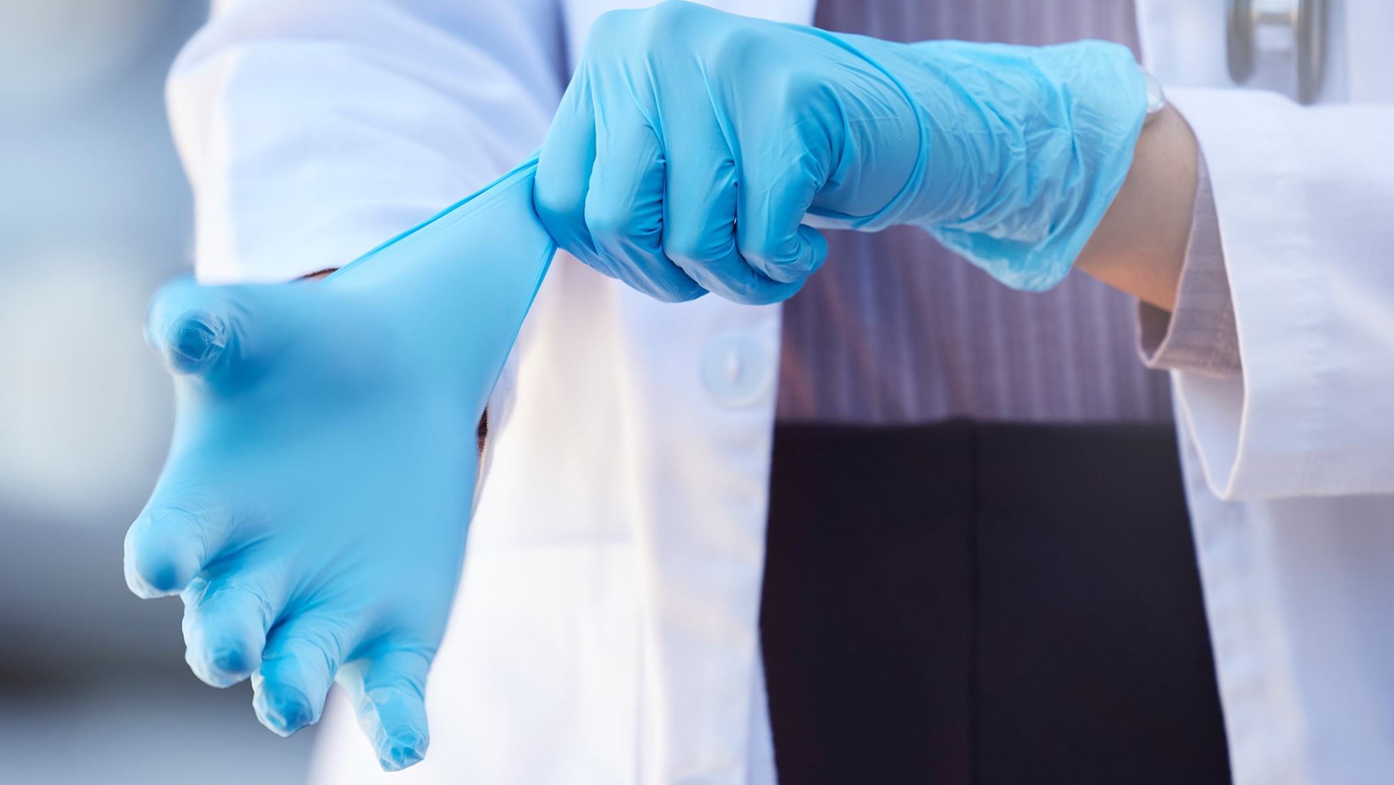 A doctor pulls on sterile gloves, only her hands showing.