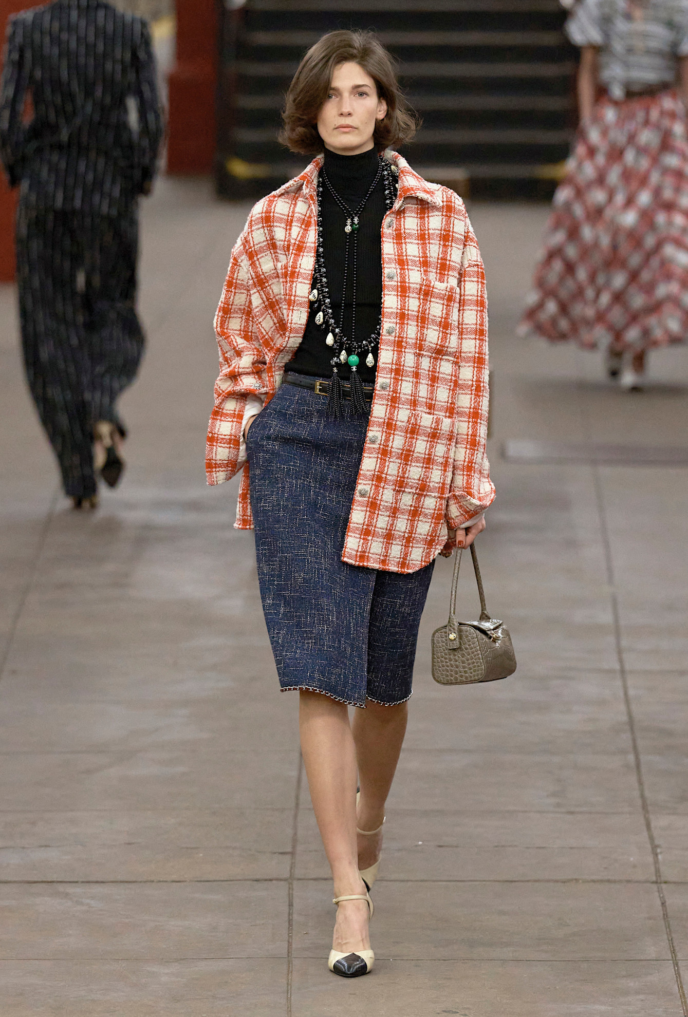 A model at the Chanel Metiers d'Art show wearing a red plaid shirt and denim pencil skirt.