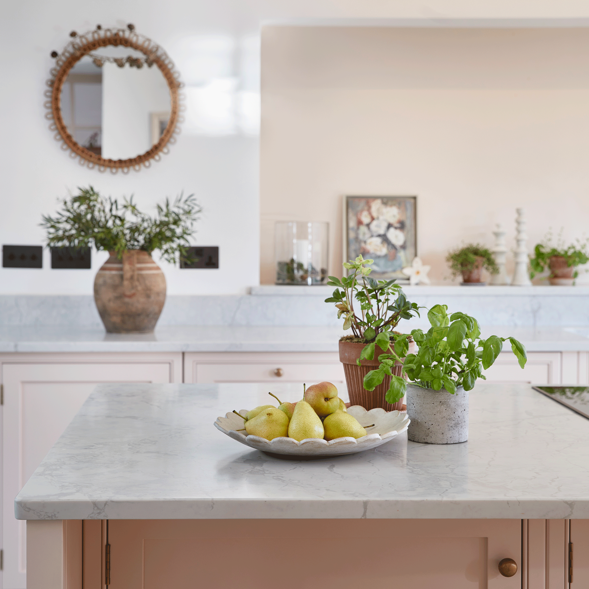 Pink kitchen with plaster pink walls, marble worktop and plant pots with herbs on worktop