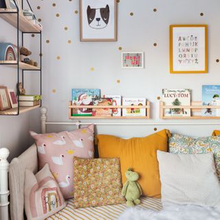Childrens room with gold decorative accent deals, hanging artork and shelving, and array of coloured cushions