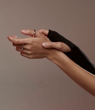 An arm held out wearing a silver ring against a pink background
